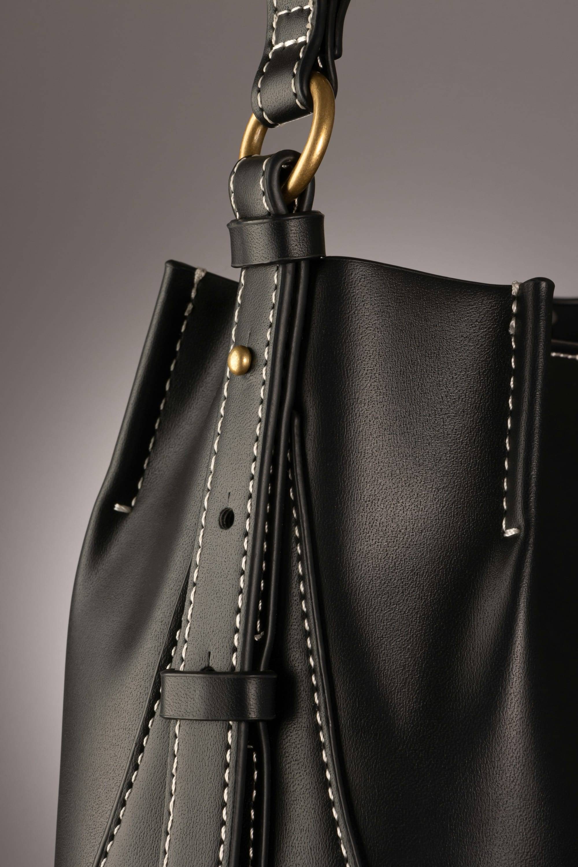 Close-up of a black leather bag with contrast stitching and a brass ring on the strap