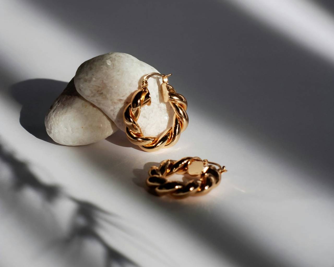 Twisted gold hoop earrings on a white stone in soft light