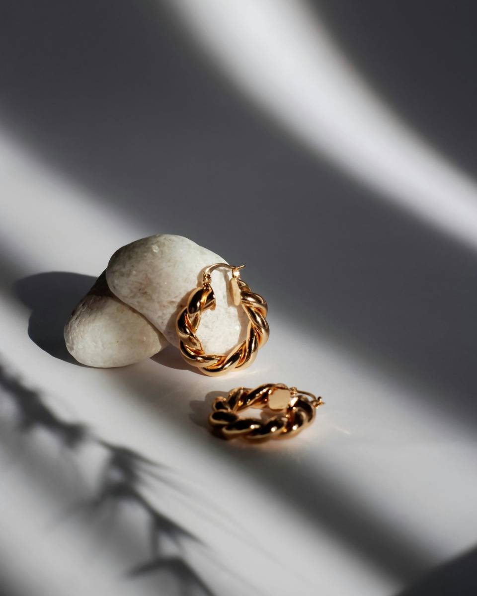 Twisted gold hoop earrings on a white stone in soft light